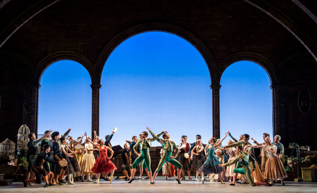 Ensemble from Act I of Don Quixote with townspeople, flamenco dancers and matadors set against a background of three large arches