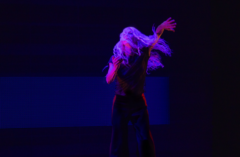 Louise Lecavalier bathed in violet light, blond hair swinging, left arm stretched out