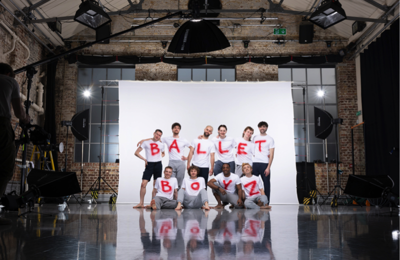 The current BalletBpoyz cohort stands in a large studio wearing white T-shirst with the company name printed on the front