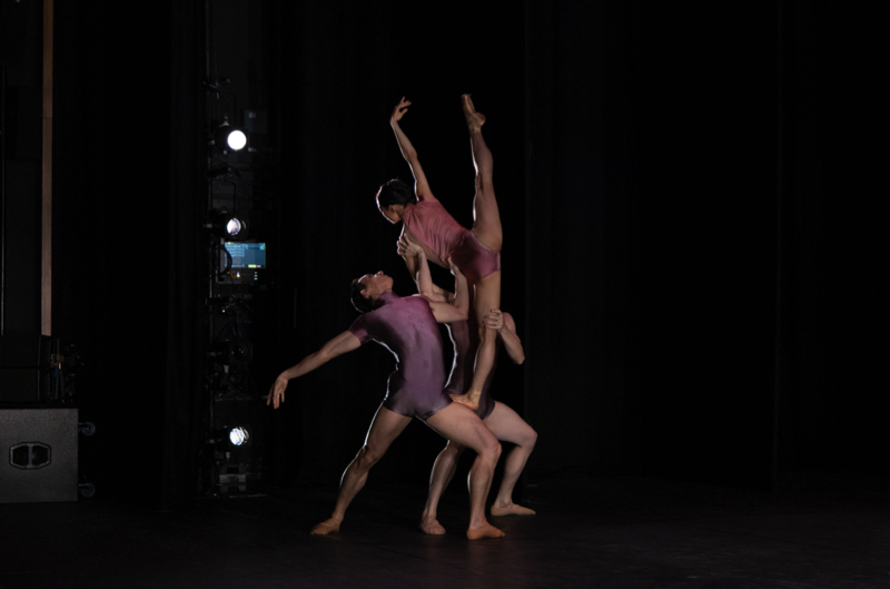 Tulsa Ballet in Divenire: two male dancers with bent knees support a female who stands on a man's thigh with one leg, the other left raised up in a 180 degree angle
