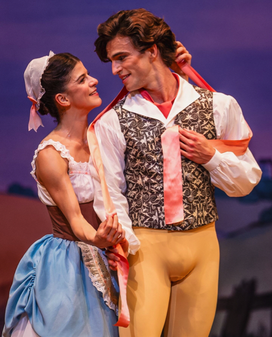 Lise, wearing a soft white cap, brown bodice and blue overskirt, cuddles Colas, who wears yellow tights and a printed waistcoat over a white shirt. They look each other in the eye and smile