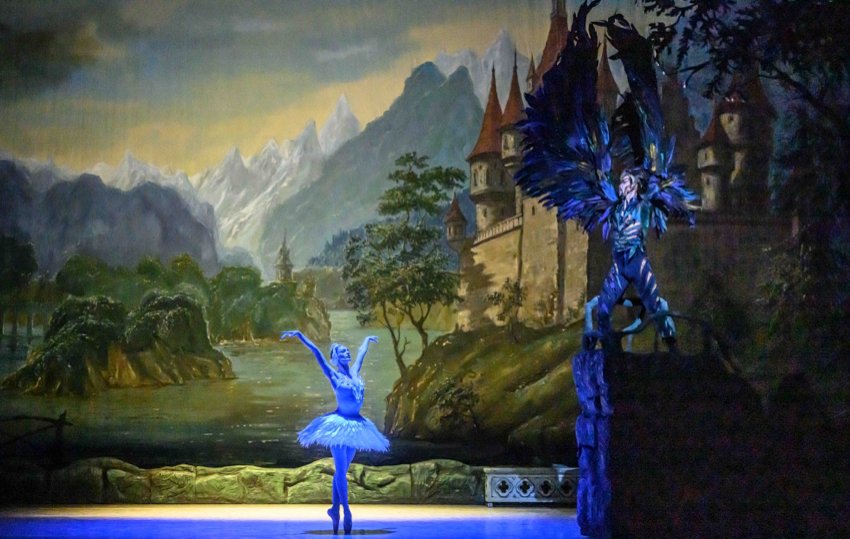 State Ballet of Georgia Swan Lake Prologue: Against a detailed backcloth depictig mountains, a ricky lake and trees, the winged Von Rothbart stands on a rocky outcrop. Below stands a woman newly transformed into a white swan