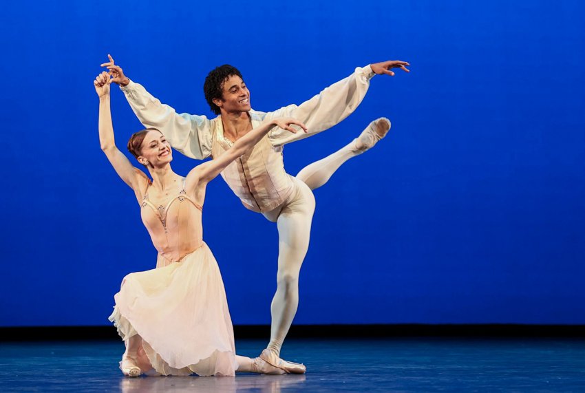 Núnez kneels on her right left, Revé stands vvehind her, right leg behind attitude, left bent. She holds his right hand. Both are smiling.