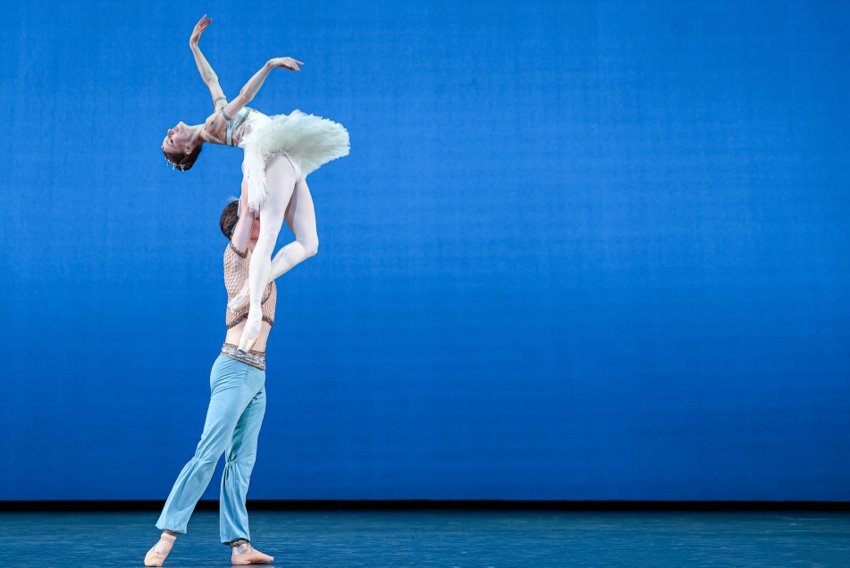 Marianela - Timeless. Muntagirov in light blue harem pants holds Núñez aloft. She ewars a white tutu and is leaning back.
