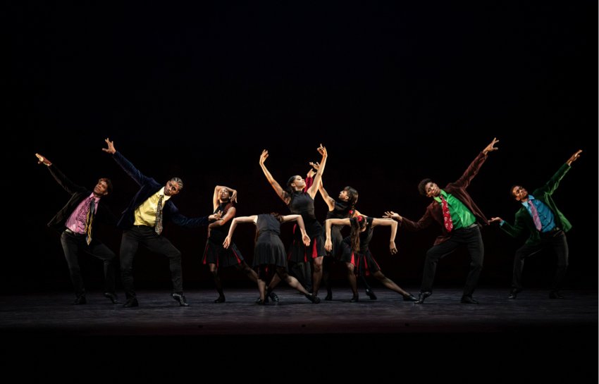 Myths and Modern Masters: An ensemble scene from Rooster: The men in colourful shirts and ties have their arms raised. A central group of women surrounds on woman with both arms raised