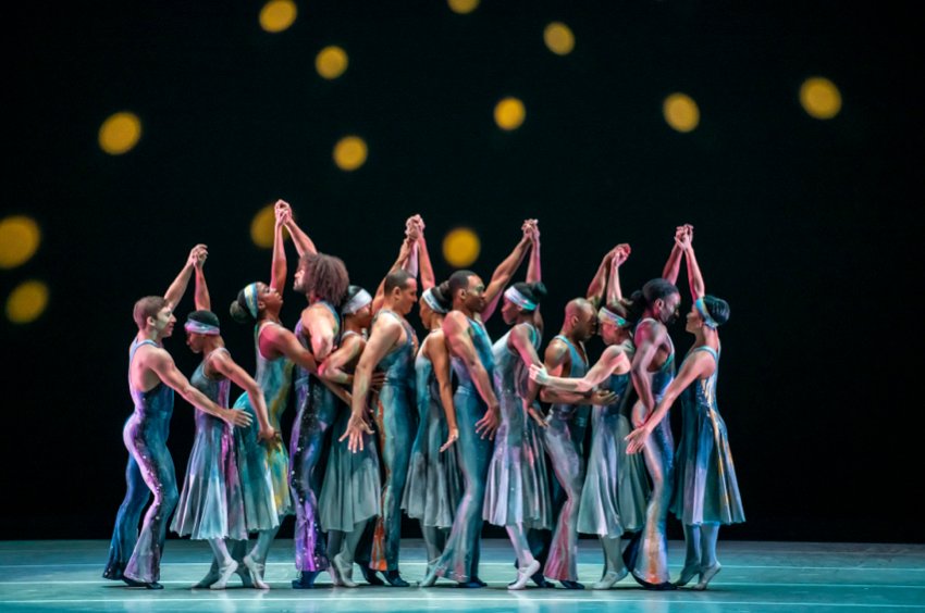 Alvin Ailey American Dance Theater, Night Creature. Pairs of dancers in jazzy shimmering blue costumes stand in line, hands held above their heads